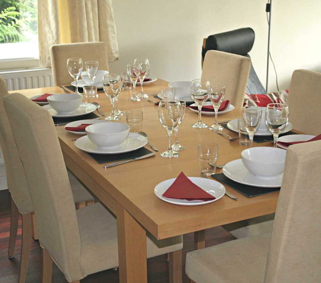 A beech coloured table set out with full place settings in white and red to show that big groups can entertain while staying at The Holt at Church Stretton.