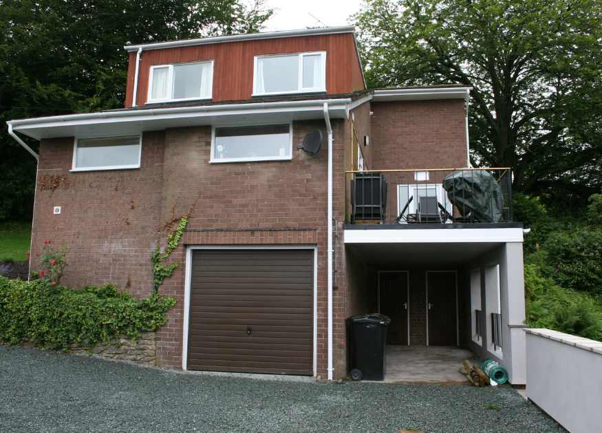 The Holt holiday cottage at Church Stretton, Shropshire, side view showing the garage, car port with bins and recycling, and the open terrace above the car port with a covered barbecue.