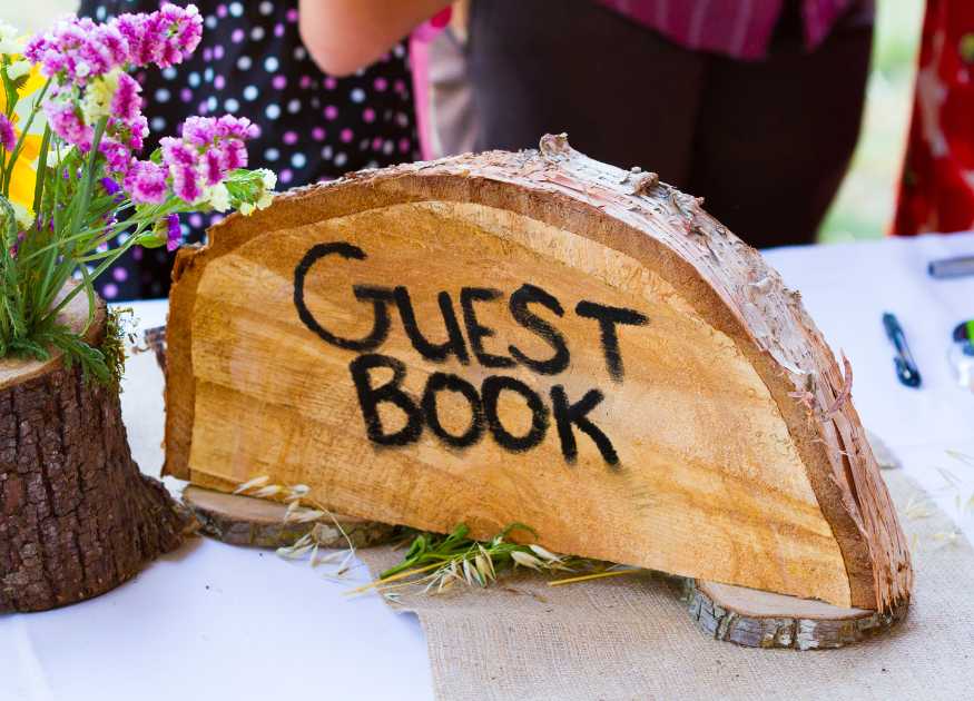 Image of a rustic half log with the words Guest Book, on table with flowers to represent the guest book page for The Holt holiday cottage