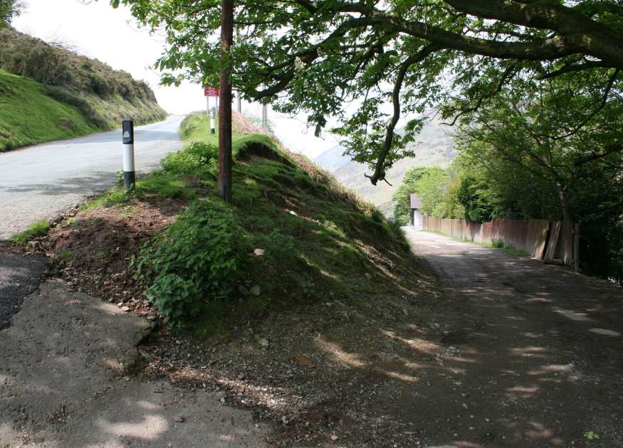 Image showing a fork in a path with a grassy knoll between the two forks, to the left is a road which curves up on to the Long Mynd hills, and to the right is a footpath which curves down to the valley, brook and National Trust cafe at Cardingmill. These are the two choices just metres from The Holt holiday cottage