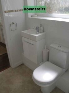 Image shows a white toilet and a white sink unit with cupboard beneath, with a door to the left and window behind. This is taken with our back to the shower unit. There is a label on the image of 