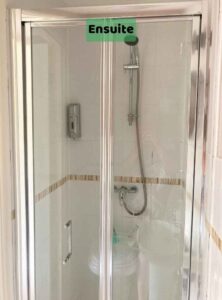 Image shows a silver single size shower cubicle with white tiles. The image is taken with our backs to the toilet end of the ensuite shown in another image. There is a label on the image of 