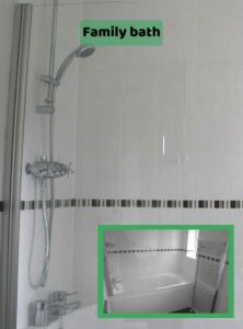 Image shows a bright white tiled shower over a bath with a glass screen and black and grey tile trim. A smaller picture is inserted in a frame below to show the landscape view of this end of the room, showing a full length bath and a heated chrome towel rail. There is a label on the image of 