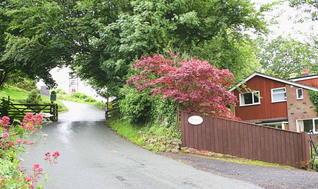 Photo showing the front fence and drive of The Holt holiday cottage, leading out on to the Burway, with the cattle grid to the Long Mynd National Park just metres away and the hills close behind.